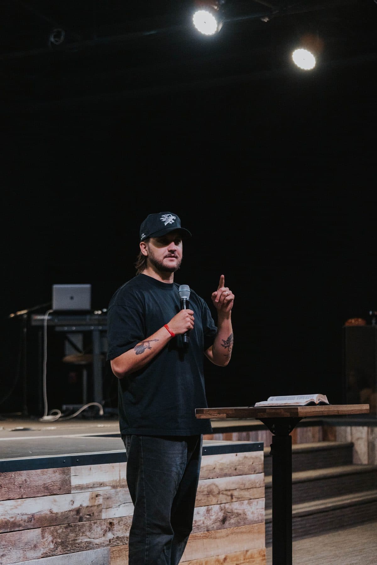 Chase preaching with a microphone, one finger raised, beside a wooden pulpit